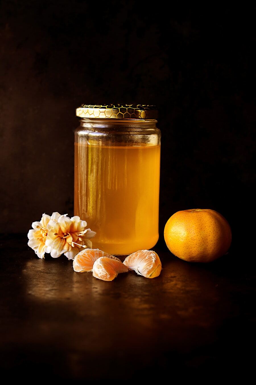 A jar of golden honey beside a naartjie