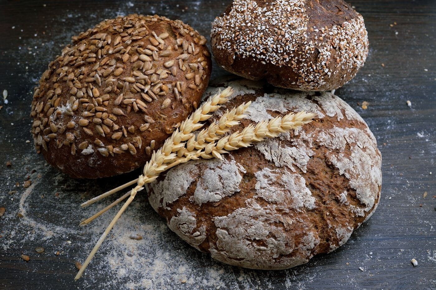 Three round, crusty loaves of dark bread with ears of wheat