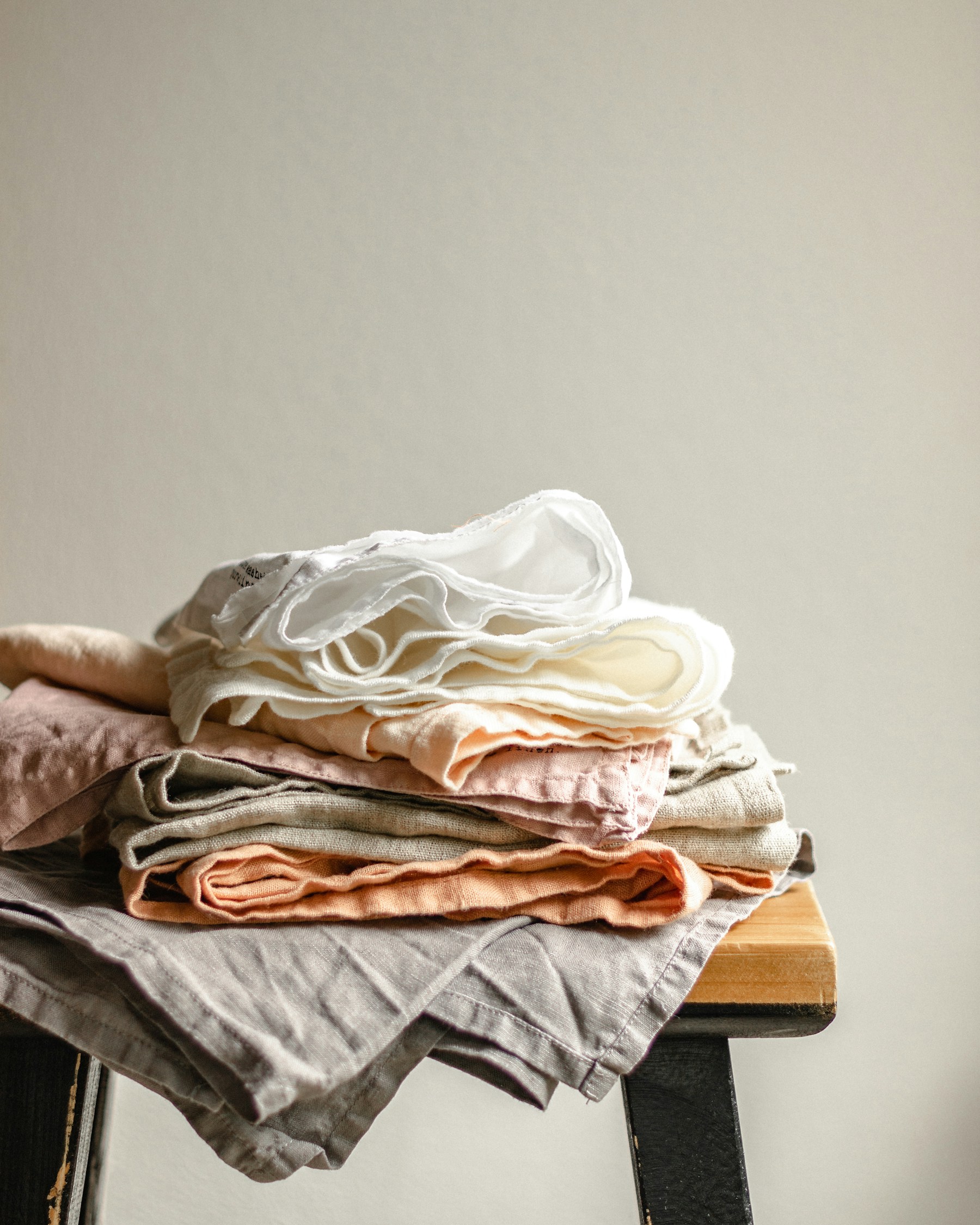 A stack of folded linen cloths in soft cream, peach and grey on a wooden table