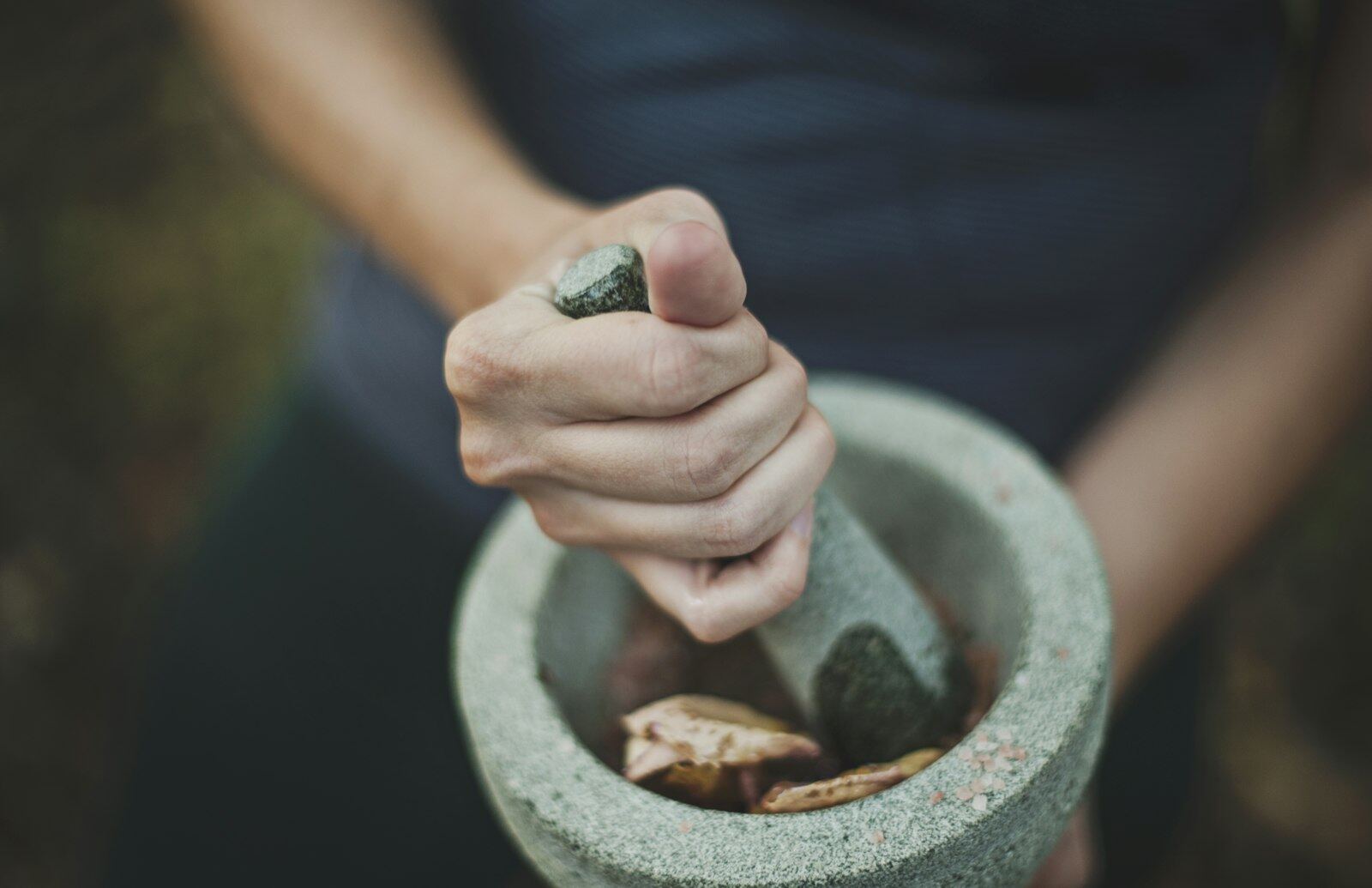 A hand grinding with a pestle in a heavy grey stone mortar