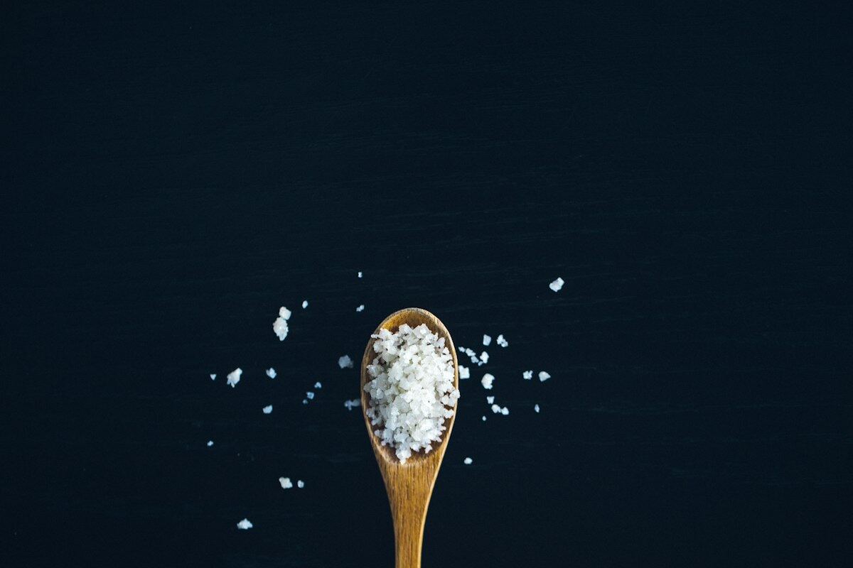 A wooden spoon of flaky sea salt on a dark background