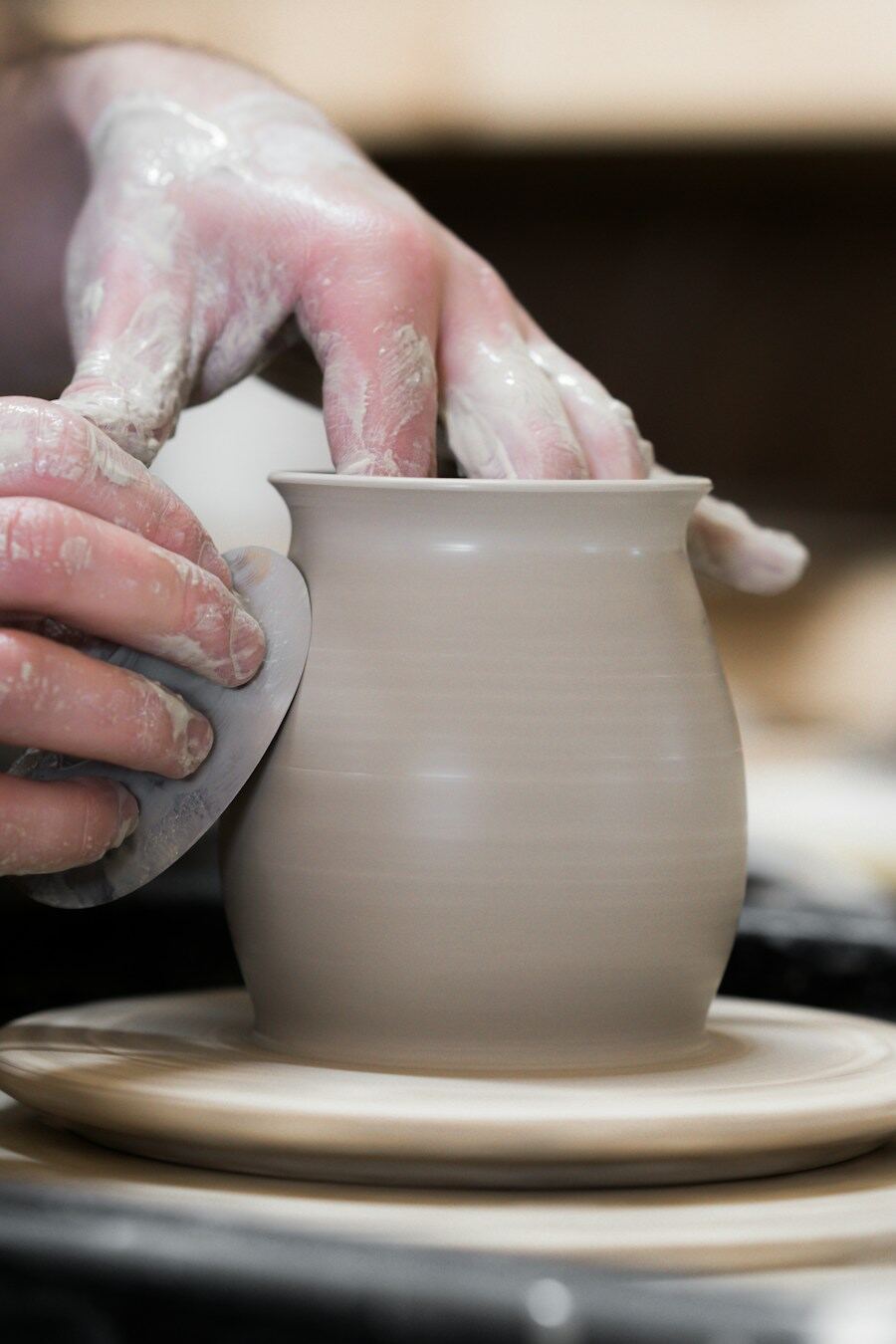 A potter’s hands shaping a clay pot on a wheel
