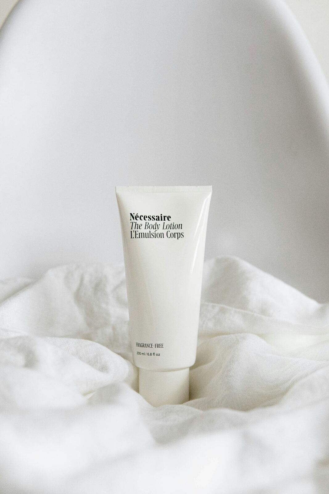 A plain white tube of body lotion standing on white linen